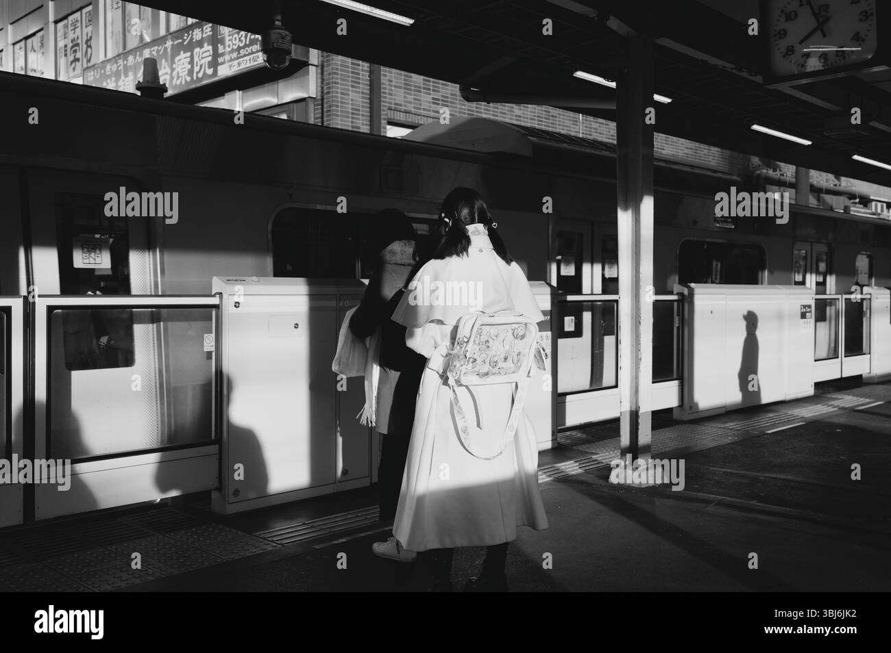 Due donne aspettano alla piattaforma di un treno di Tokyo, il sole getta lunghe silhouette in bianco e nero Foto Stock