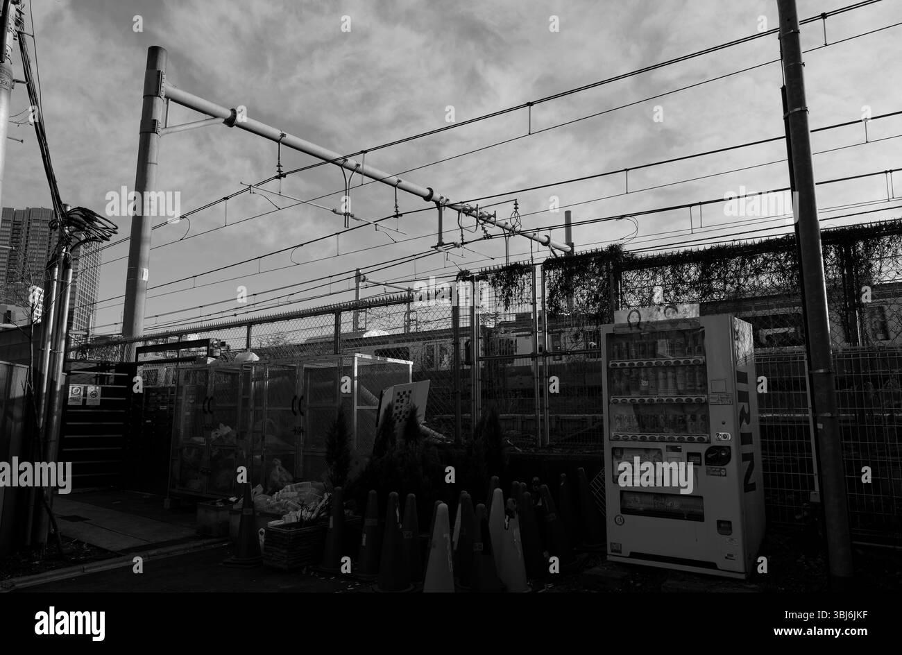 Fili aggrovigliati, coni stradali usurati e un distributore automatico solitario: Natura morta urbana sotto i binari dei treni di Tokyo a Ōkubo Foto Stock