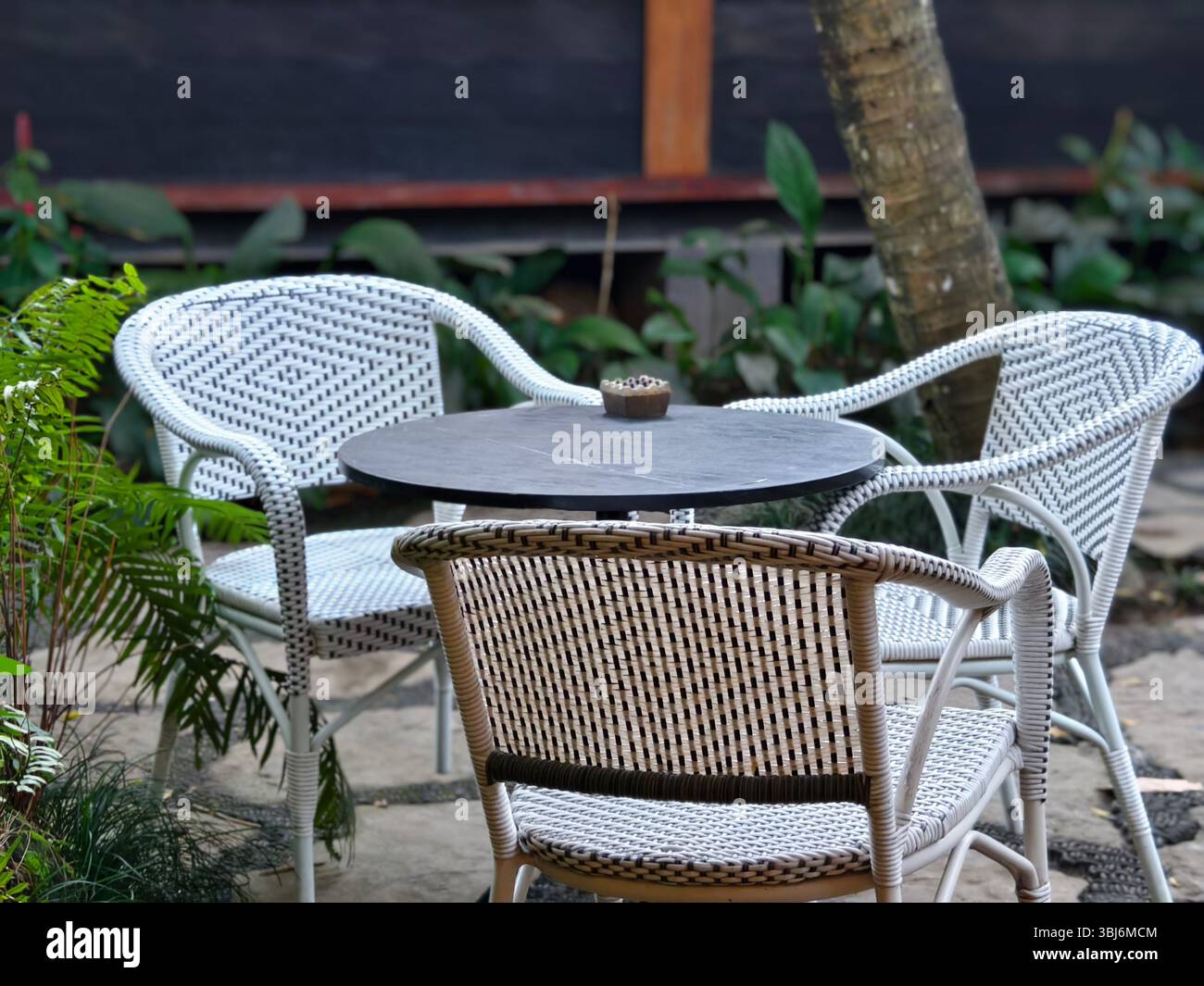 Un set di sedie in rattan intrecciato e un tavolo rotondo in un caffè giardino Foto Stock