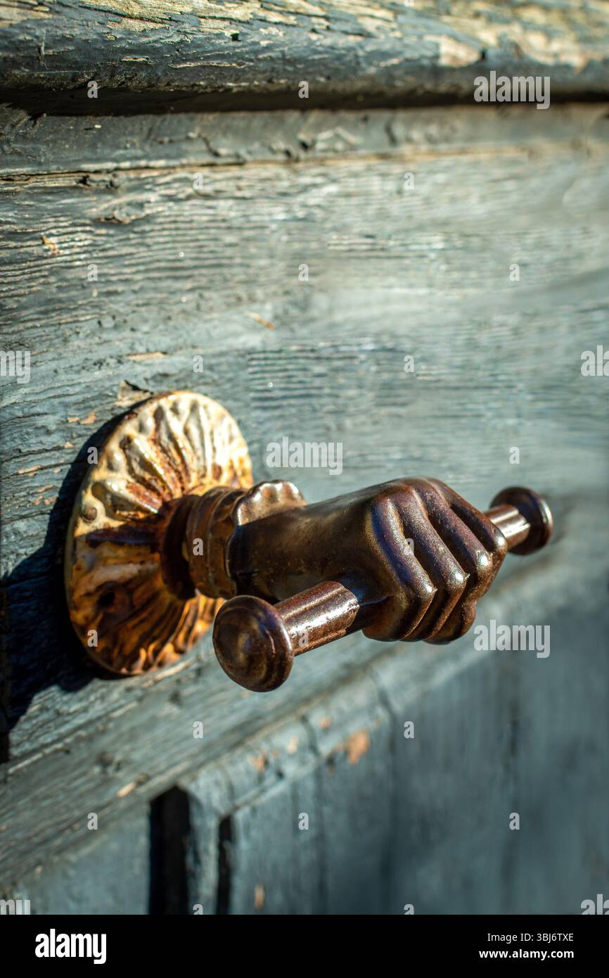 Una caratteristica maniglia della portiera che ricorda una maniglia a mano afferra una porta in legno rustico, caratterizzata da dettagli intricati e un'affascinante patina. Francia Foto Stock