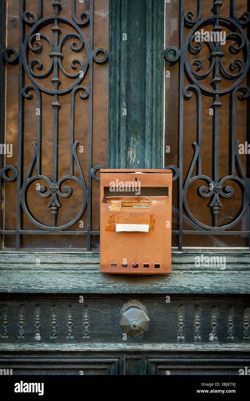 Una cassetta postale arrugginita è fissata a una porta in ferro battuto splendidamente lavorata. L'intricato lavoro in ferro contrasta con il legno intemprato. Auvergne. Francia Foto Stock