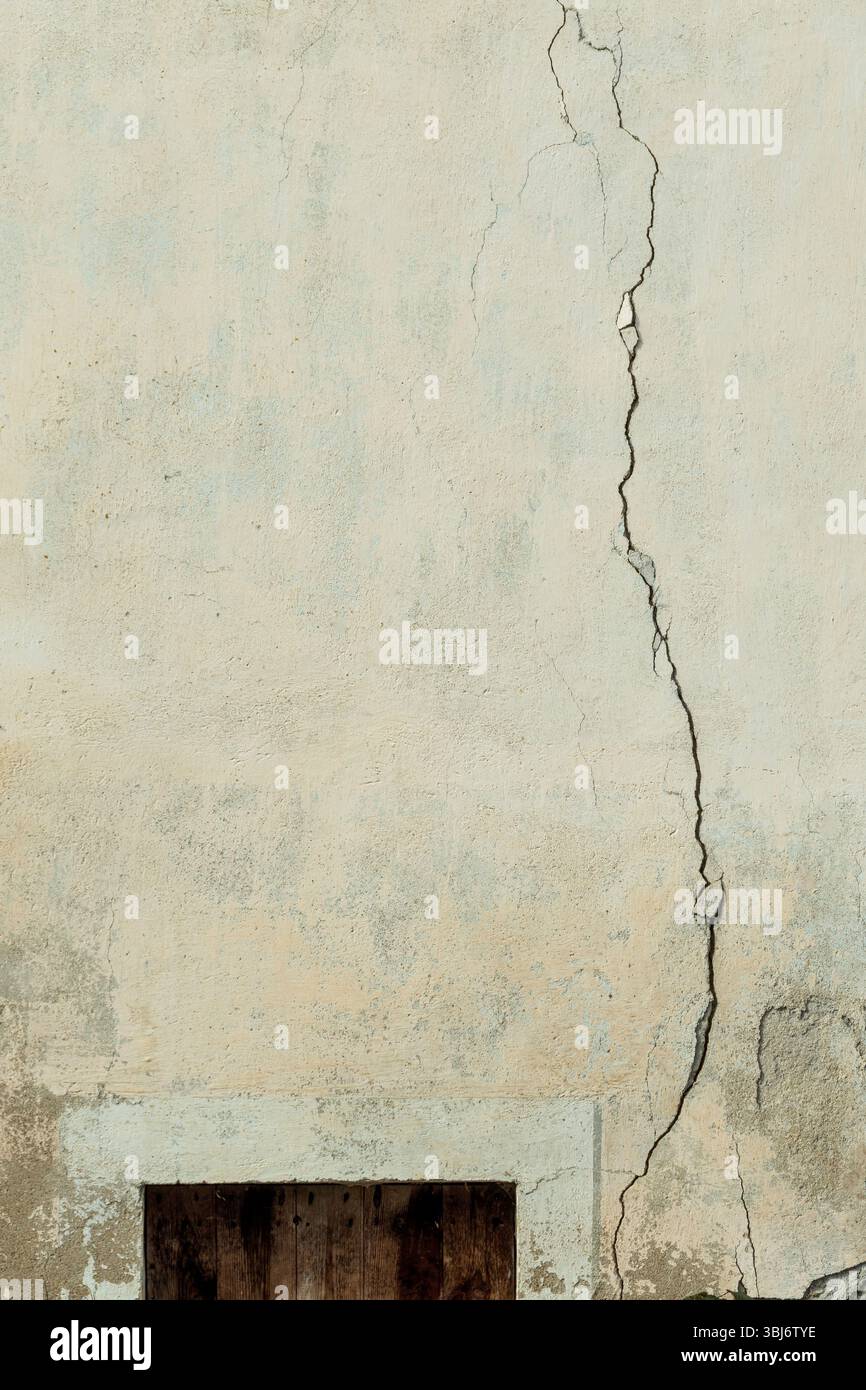 Una superficie della parete incrinata mostra il passaggio del tempo con usura visibile. La texture mette in risalto il gioco di luci e ombre, a indicare un ambiente urbano. Foto Stock