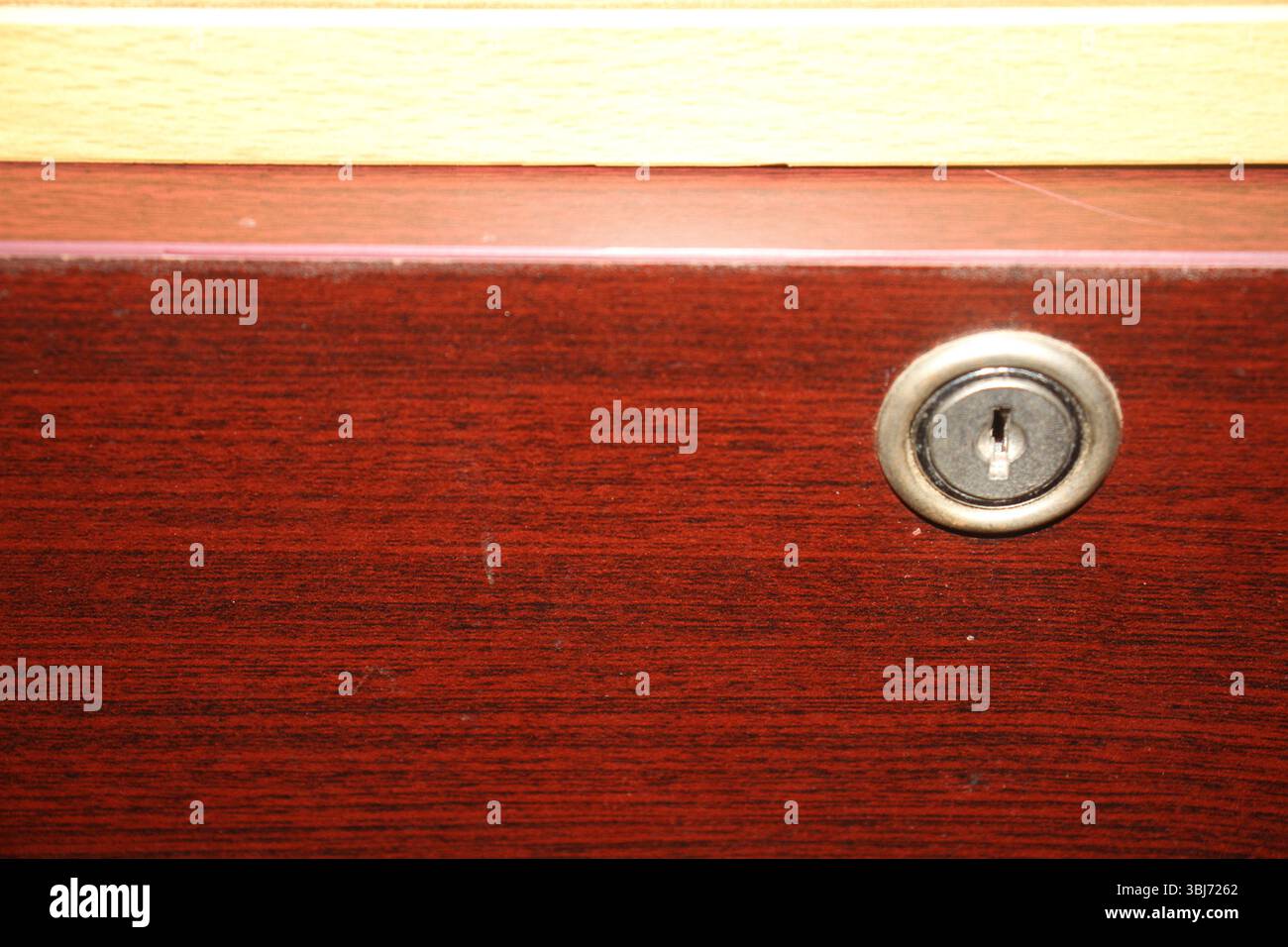 Vista ravvicinata di un cassetto in legno con serratura circolare metallica incorporata nella sua superficie. Il legno ha una finitura marrone rossastro lucido. Foto Stock