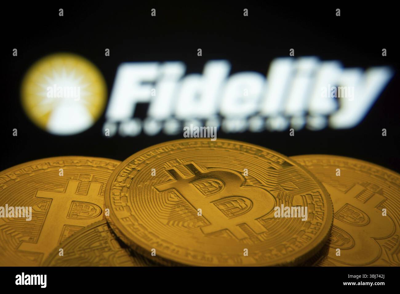 Dacca, Bangladesh- 12 giugno 2025: Primo piano delle monete Bitcoin con il logo Fidelity Investments visibile su uno schermo sullo sfondo Foto Stock