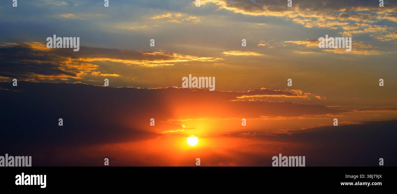 Spettacolare sfondo al tramonto con sole luminoso, cielo blu e nuvole pittoresche. Foto Stock