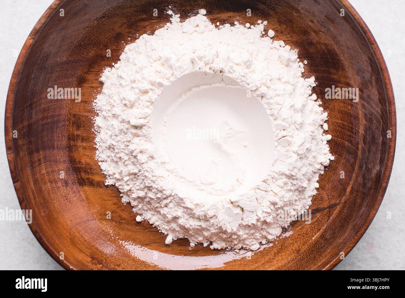 Vista dall'alto della farina multiuso in un recipiente, vista dall'alto della farina da forno su un piano di lavoro bianco Foto Stock