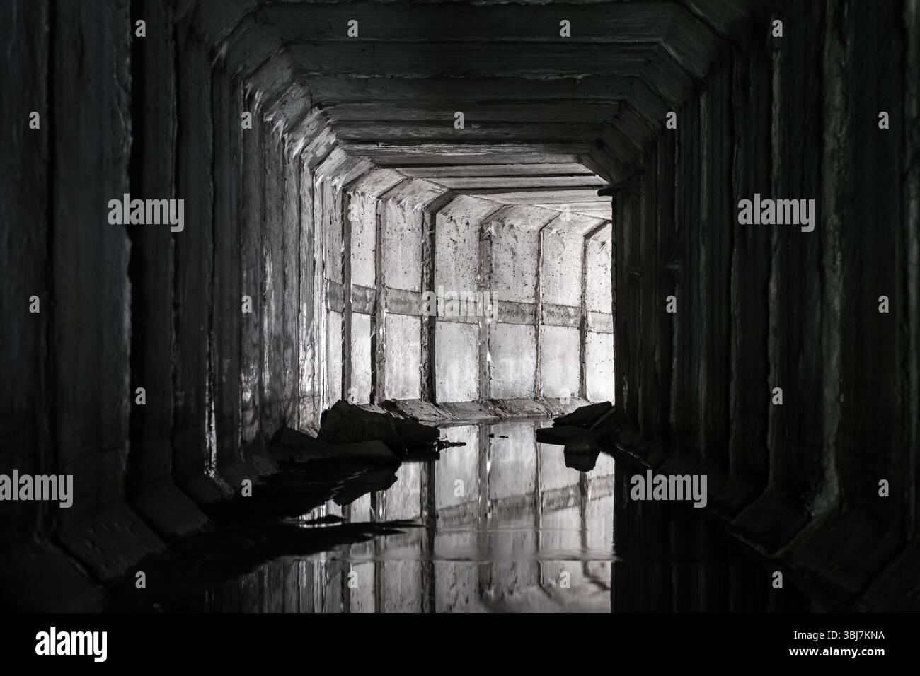 Un tunnel di drenaggio quadrato in cemento con una luce all'estremità che splende dalla curva del tunnel. Foto Stock
