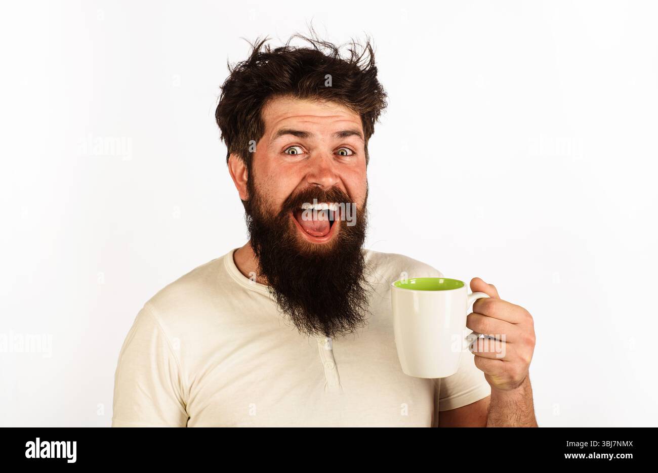 Uomo barbuto felice con una tazza di tè o caffè. Bell'uomo con tazza di bevanda calda. Uomo che beve caffè mattutino o tè. Bearded Guy in t-shirt bianca con Foto Stock