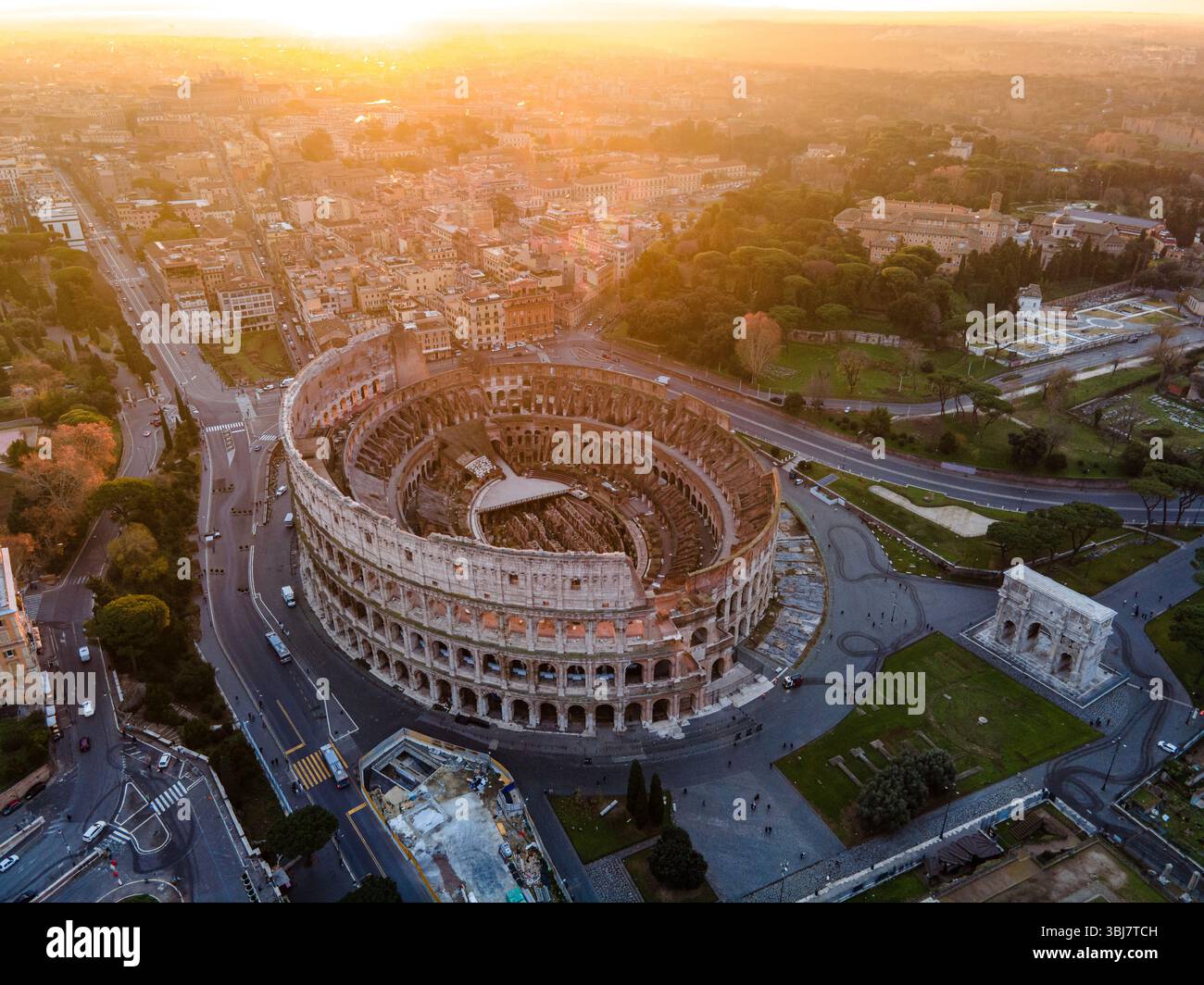 Vista aerea del Colosseo a Roma, in Italia, completamente visibile ad angolo durante l'alba, con un cielo arancione che emette una calda luce mattutina. Foto Stock