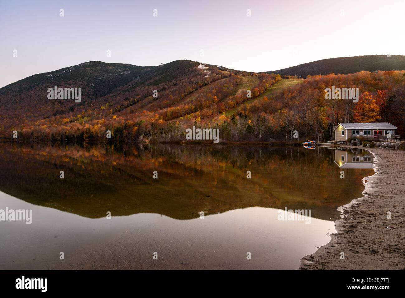 Montagna boscosa al culmine del fogliame autunnale che si riflette nelle acque calme di un lago al crepuscolo Foto Stock