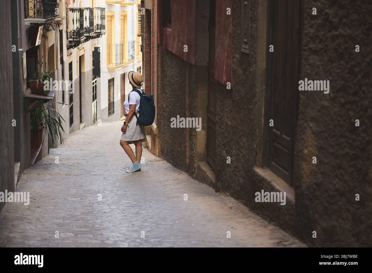 Un viaggiatore che percorre affascinanti e strette strade europee con architettura medievale, abbracciando cultura ed esplorazione. Ideale per argomenti di tradizione, da a. Foto Stock