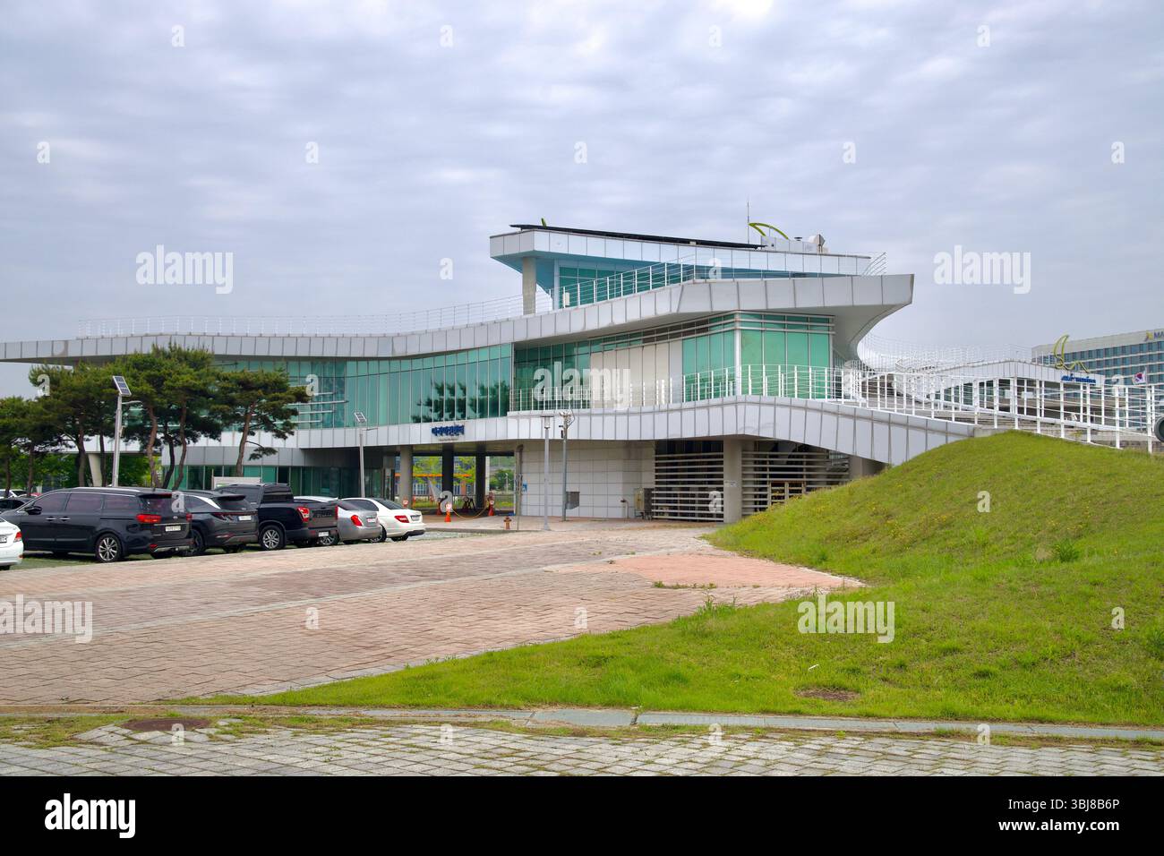 Incheon, Corea del Sud - 19 maggio 2025: Una moderna struttura rivestita di vetro presso l'Ara Marina presenta vialetti sul tetto e giardini inclinati accanto ad una piccola pa Foto Stock