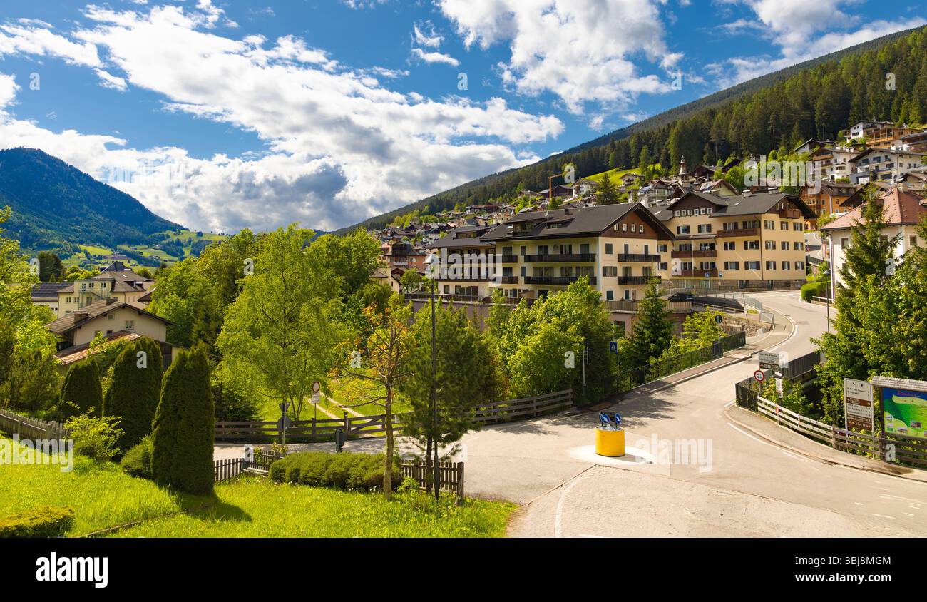 Una vista aerea di Ortisei, un pittoresco villaggio alpino nelle Dolomiti, caratterizzato da edifici tradizionali incastonati su una collina con lussureggianti alberi verdi Foto Stock
