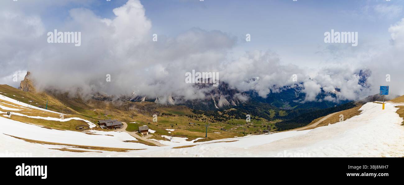 Vista panoramica da Seceda, Dolomiti, con spettacolari nuvole che si snodano intorno a aspre vette, copertura parziale della neve e verdi vallate. Foto Stock