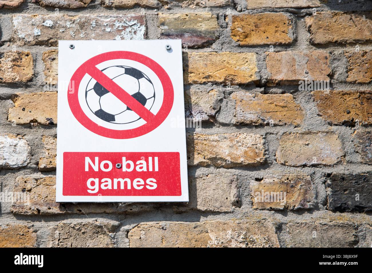 Cartello No Ball Games montato su una parete di mattoni, con un cerchio rosso e una linea sopra il simbolo di una palla, comunemente visto nelle aree residenziali del Regno Unito. Foto Stock