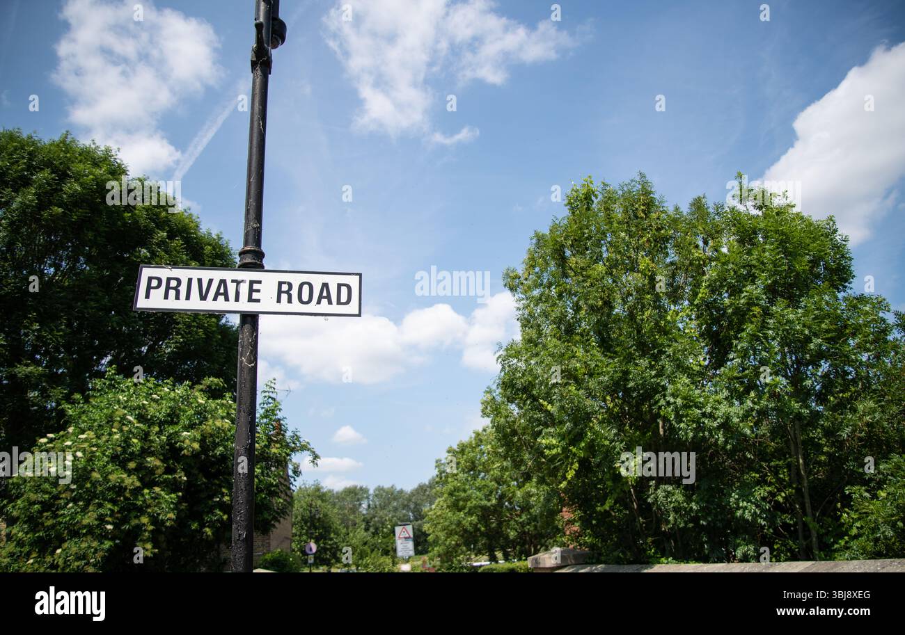 Cartello stradale privato con testo bianco su sfondo nero, sullo sfondo di lussureggianti alberi verdi su una tranquilla strada rurale. Foto Stock