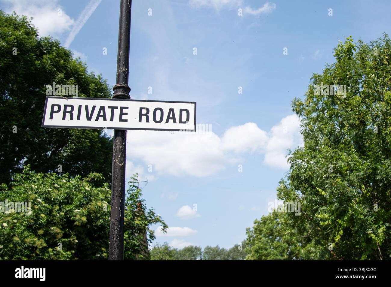 Cartello stradale privato con testo bianco su sfondo nero, sullo sfondo di lussureggianti alberi verdi su una tranquilla strada rurale. Foto Stock