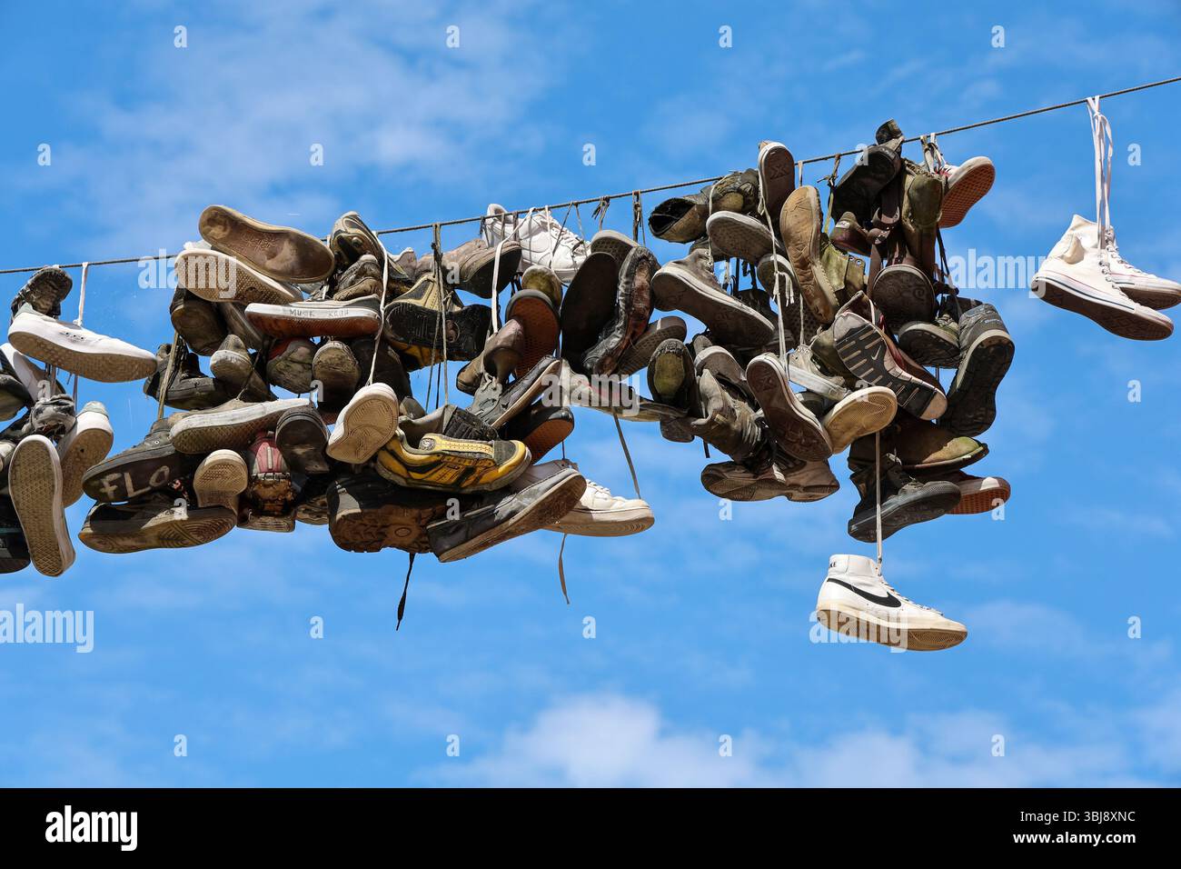 Flensburg, Germania - 13. Giugno 2025: Scarpe da ginnastica indossate appese a un filo a Flensburg, creando un'immagine unica sullo sfondo di un cielo azzurro Foto Stock