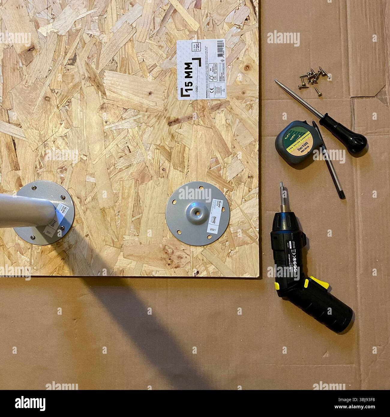 Scenario di miglioramento domestico con banco MDF in corso, utensili e materiali sul pavimento, tra cui trapano, metro a nastro, bradawl e matita - Immagine stock catturata con smartphone