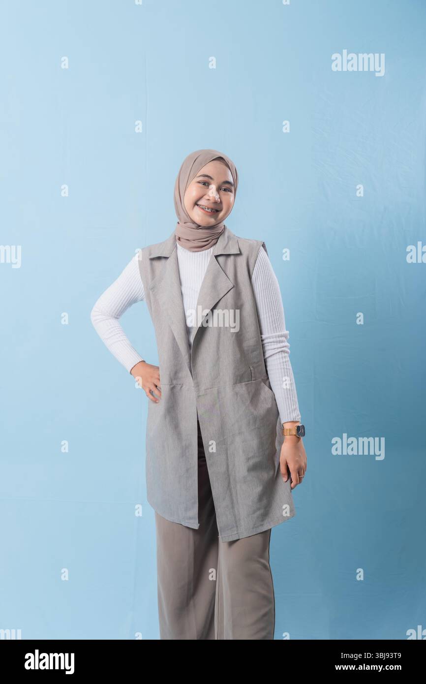 Una donna che indossa un gilet grigio e una camicia bianca sorride alla telecamera. Indossa un velo e ha le braccia incrociate Foto Stock