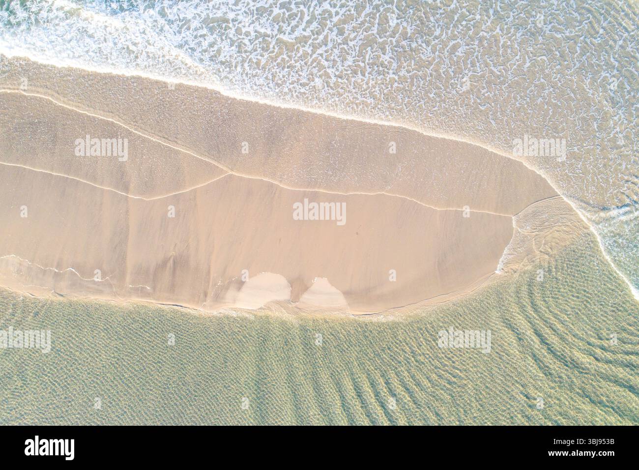 ripresa con drone che cattura gli intricati motivi di schiuma bianca su una costa incontaminata, immagine aerea dall'alto verso il basso dal drone Foto Stock