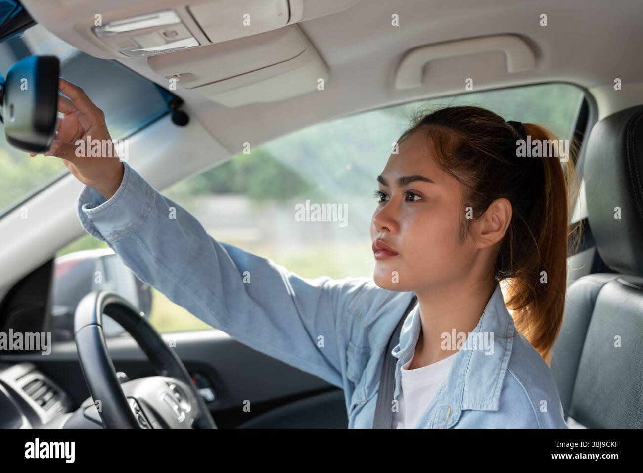 donna regola lo specchietto retrovisore dell'auto prima della guida, guida con intento, guida sicura, pratica di guida, donna allegra seduto comodamente sul sedile del conducente wi Foto Stock