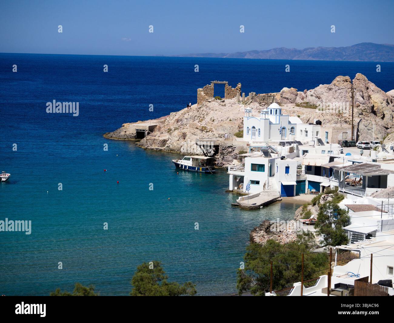 Firopotamos sull'Isola di Milos con case bianche e finestre blu incorniciate da calme acque turchesi sotto il cielo azzurro. Un tranquillo villaggio delle Cicladi. Foto Stock