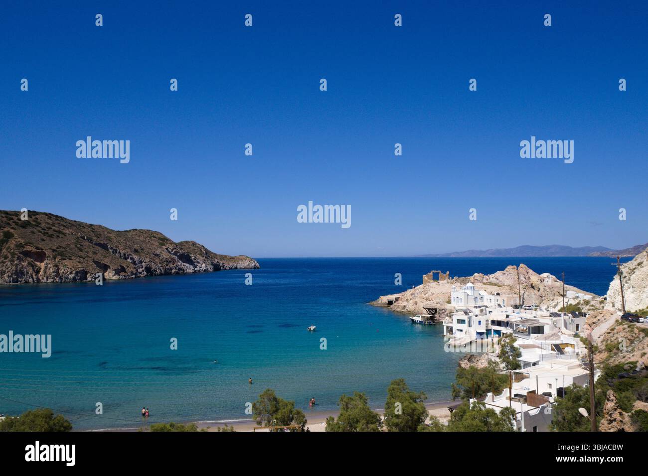 Distante vista panoramica della baia di Firopotamos su Milos con case delle Cicladi, mare turchese calmo e cielo azzurro limpido in una tranquilla giornata estiva. Foto Stock