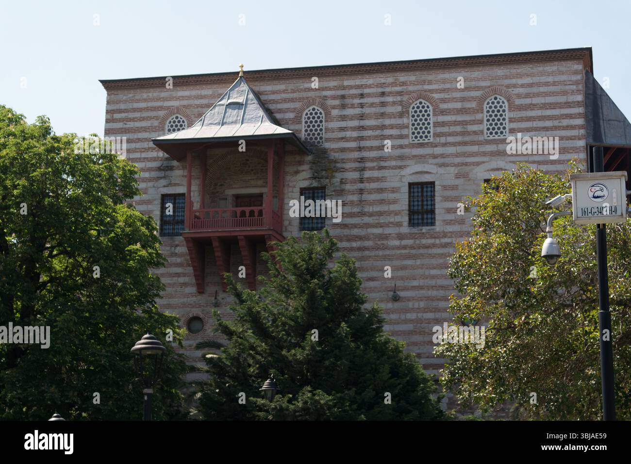 I visitatori ammirano le caratteristiche architettoniche uniche di un edificio storico di Istanbul, circondato da alberi e bagnato dalla luce del sole. Foto Stock