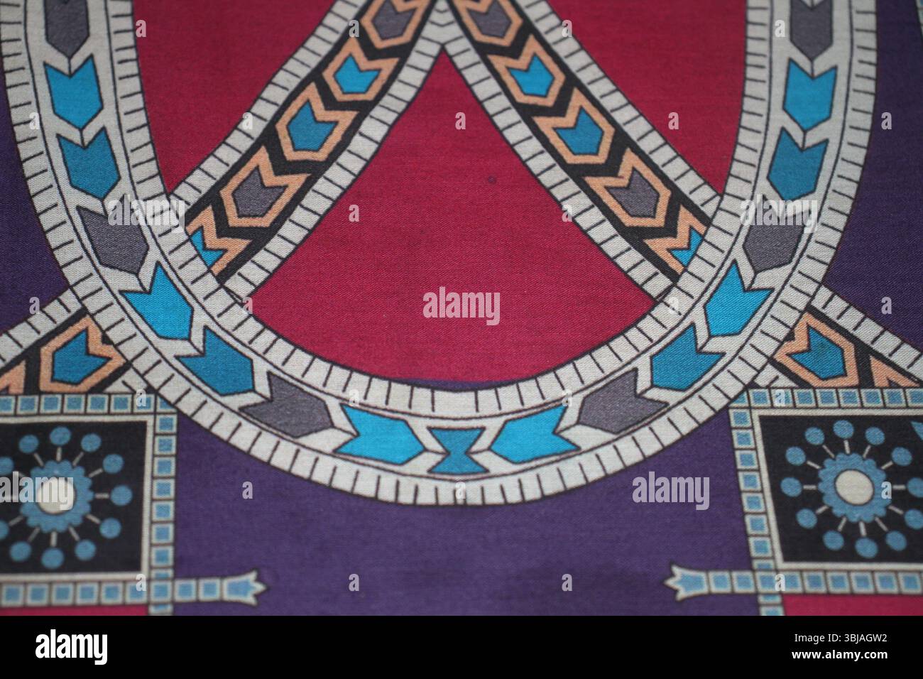 Un design in tessuto vivace con motivi geometrici intrecciati in ricche tonalità di rosso, blu, viola, pesca, nero, e bianco. Foto Stock