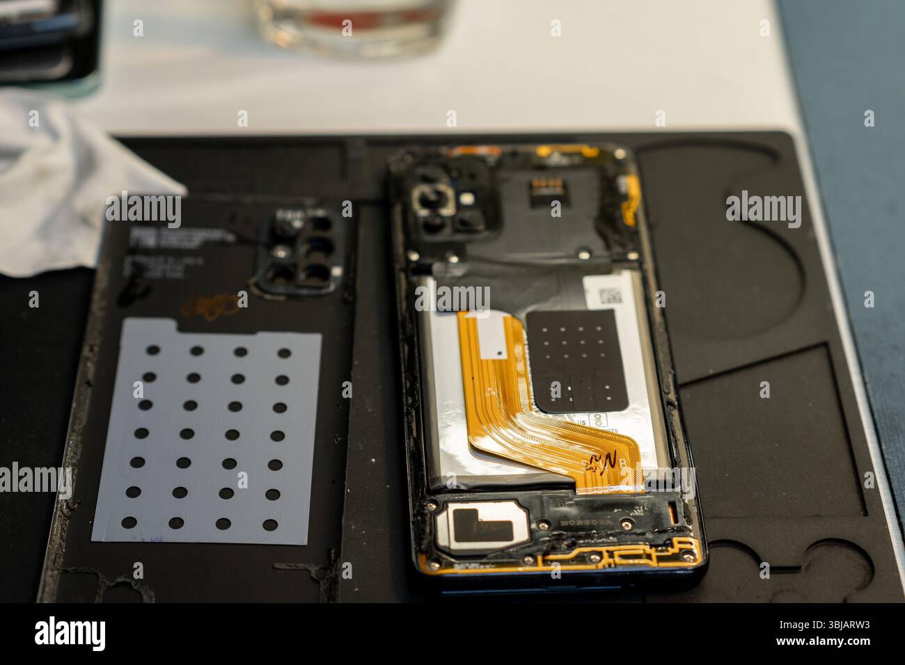 Il tecnico lavora su uno smartphone aperto, esponendo i componenti interni e preparandosi per le riparazioni in un'officina di riparazione telefonica affollata durante le ore diurne Foto Stock