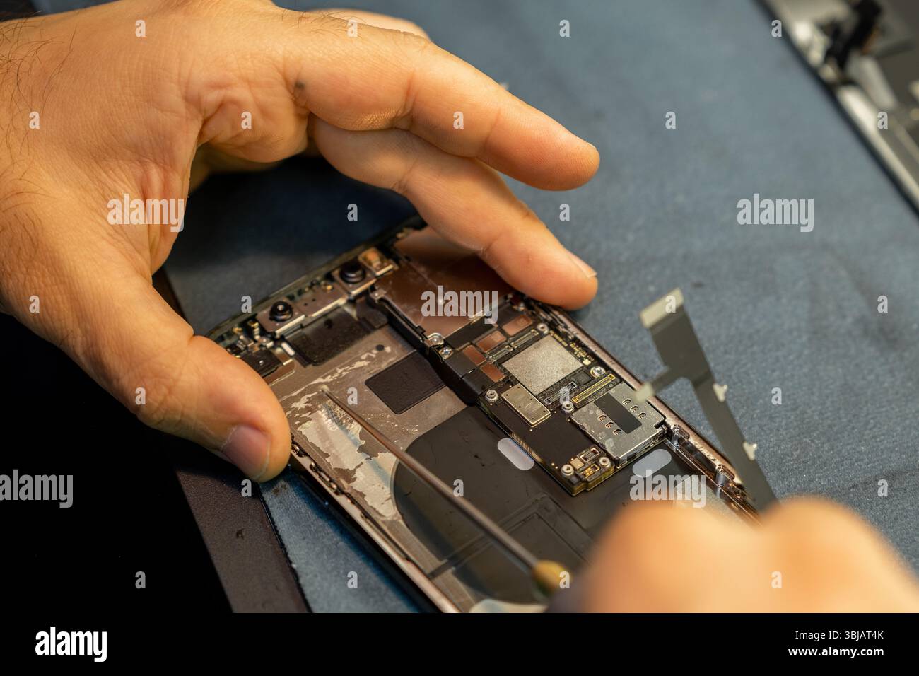 Il tecnico ripara abilmente uno smartphone, concentrandosi sulle parti interne e utilizzando strumenti di precisione in un ambiente di officina moderno. Foto Stock