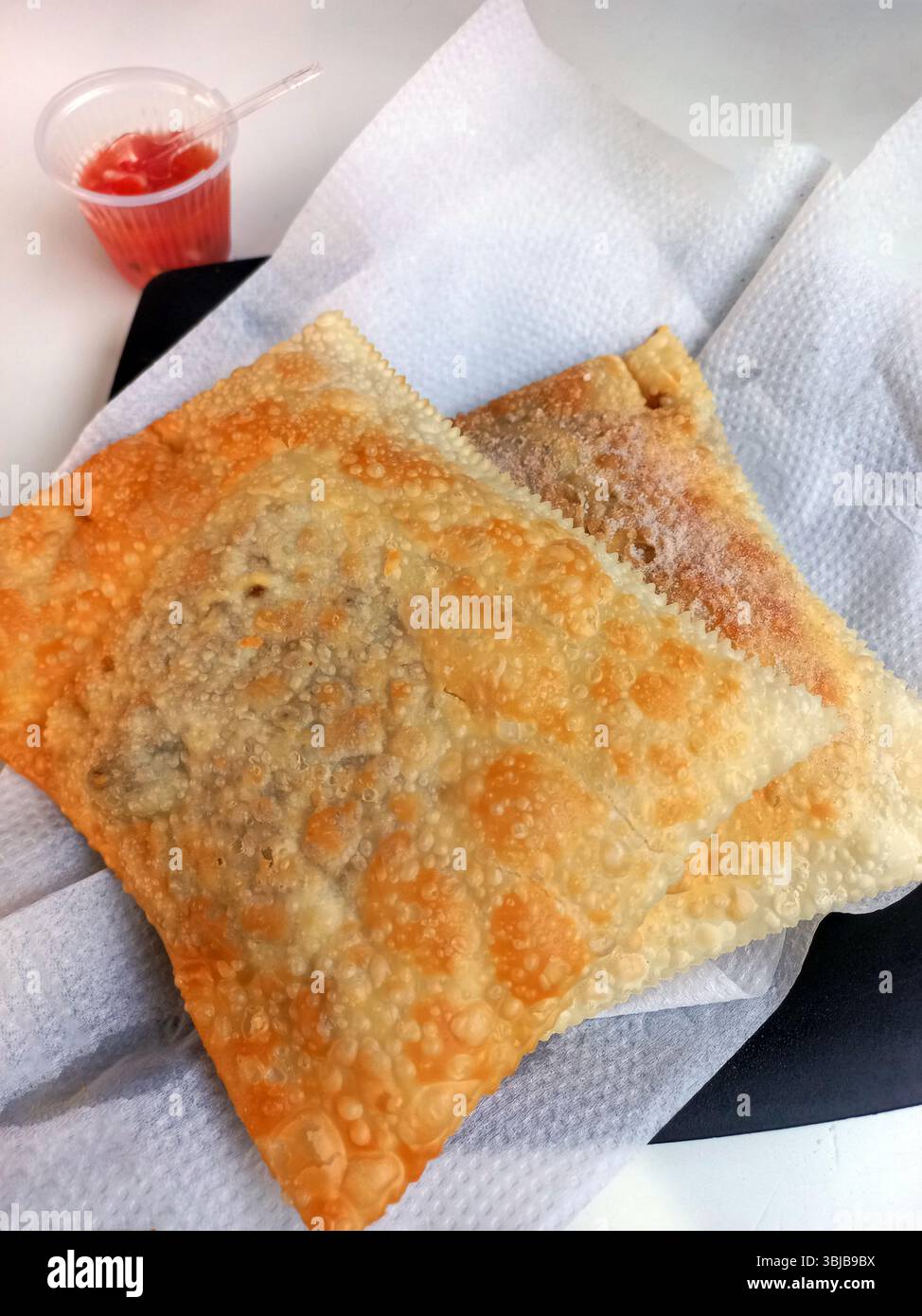 Pastello dorato croccante servito su tovagliolo con una piccola tazza di plastica di salsa rossa tipica dei mercati di Street food brasiliani e bancarelle di snack Foto Stock