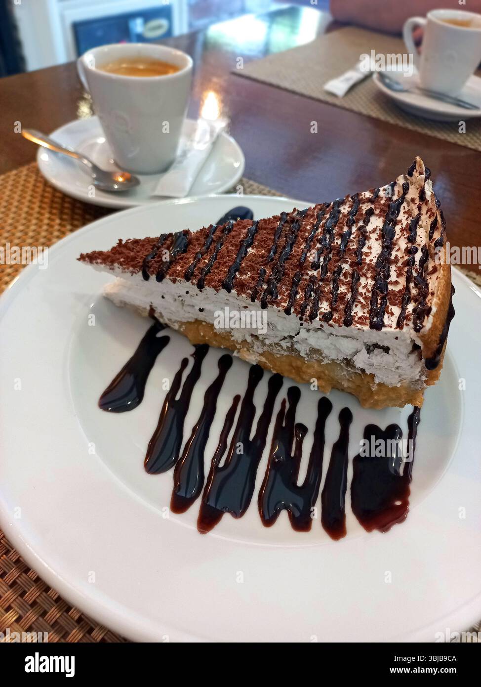 Deliziosa fetta di dessert al cioccolato con strati cremosi e gocce di cioccolato abbinato a un espresso caldo su un piatto bianco Foto Stock