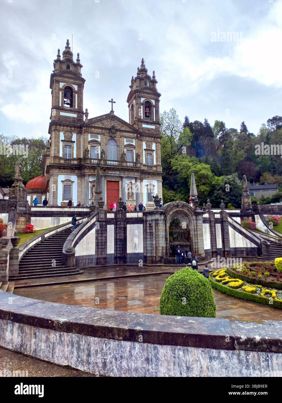 Braga Portogallo marzo 29 2024 chiesa barocca di Bom Jesus do Monte con i visitatori che scalano scale e aiuole in primo piano Foto Stock