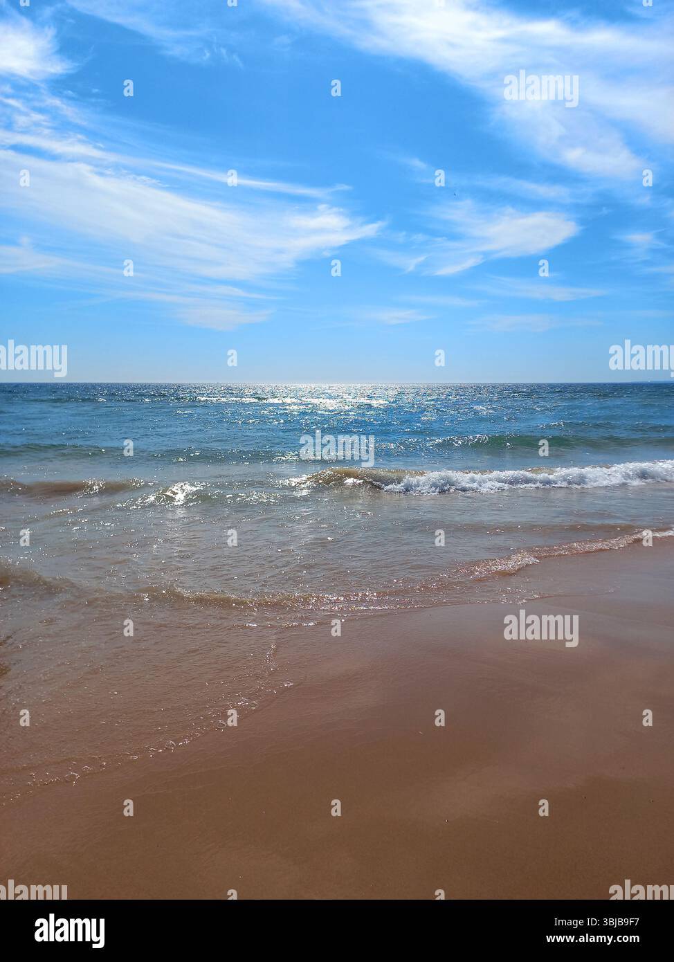 Tranquilla vista sull'oceano con onde morbide che raggiungono la sabbia dorata sotto un vivace cielo blu alla spiaggia fonte da Telha in Portogallo Foto Stock