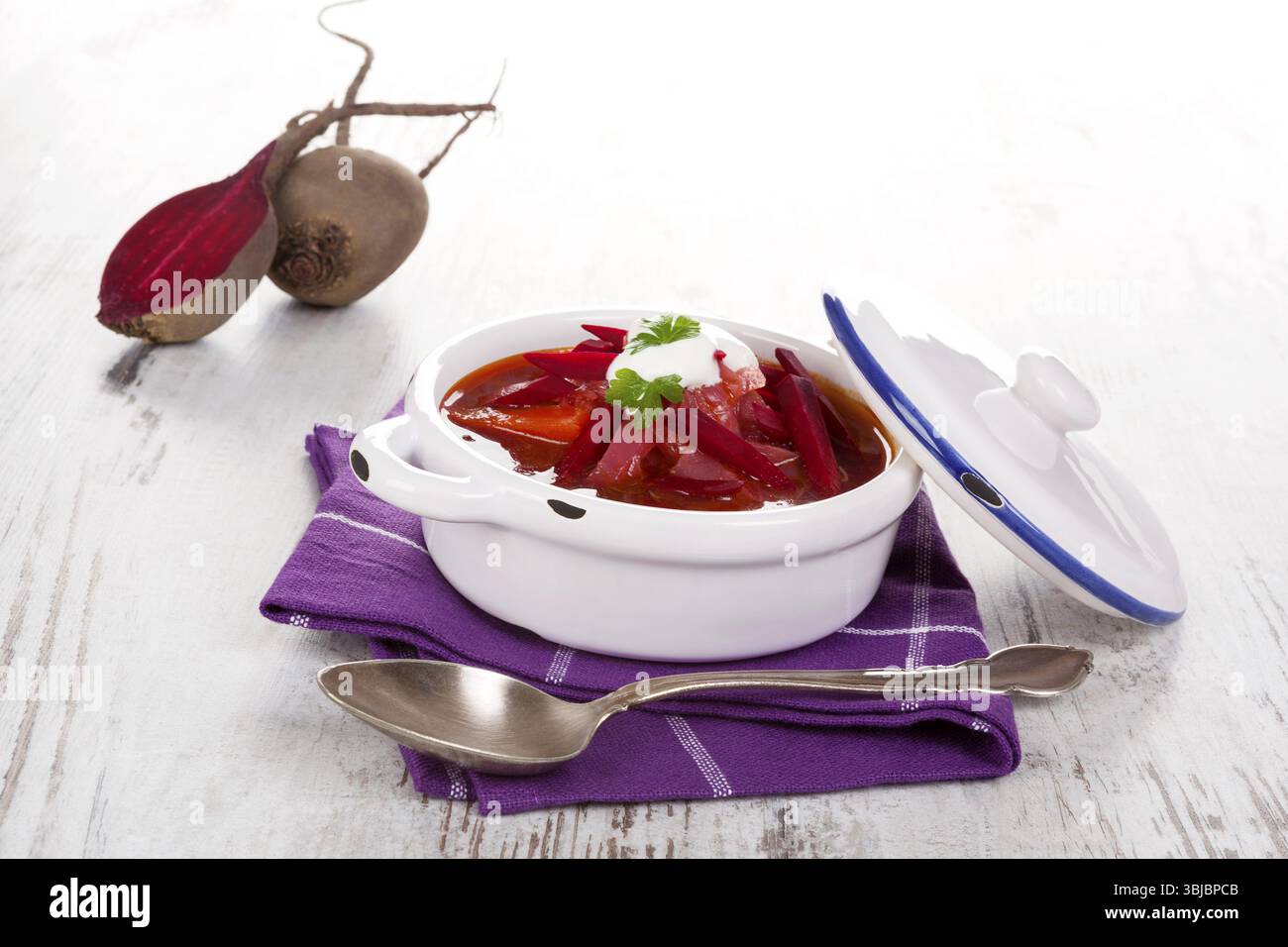 Deliziosa zuppa borsch ucraina con verdure fresche di barbabietola su un panno viola su un tavolo rustico in legno. Cucina tradizionale europea Foto Stock