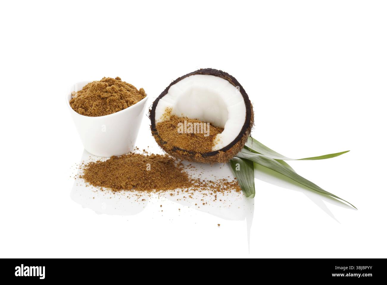 Fondo di zucchero di cocco. Una sana alternativa allo zucchero. Metà di cocco, foglie di palma e zucchero di cocco di canna isolato su fondo bianco Foto Stock