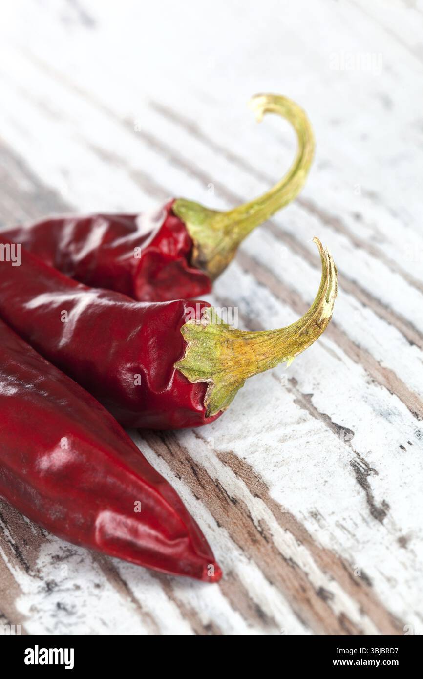 Sfondo peperoncino di lusso. Tre peperoncini secchi su fondo bianco testurizzato in legno. Ingredienti per cucinare a caldo Foto Stock