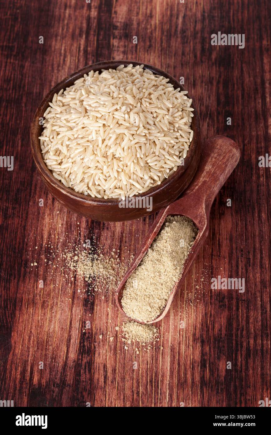 Riso in una ciotola rotonda di legno con fibra di riso dietetica su un cucchiaio di legno su fondo di legno marrone scuro, vista dall'alto. Concetto di alimentazione sana Foto Stock