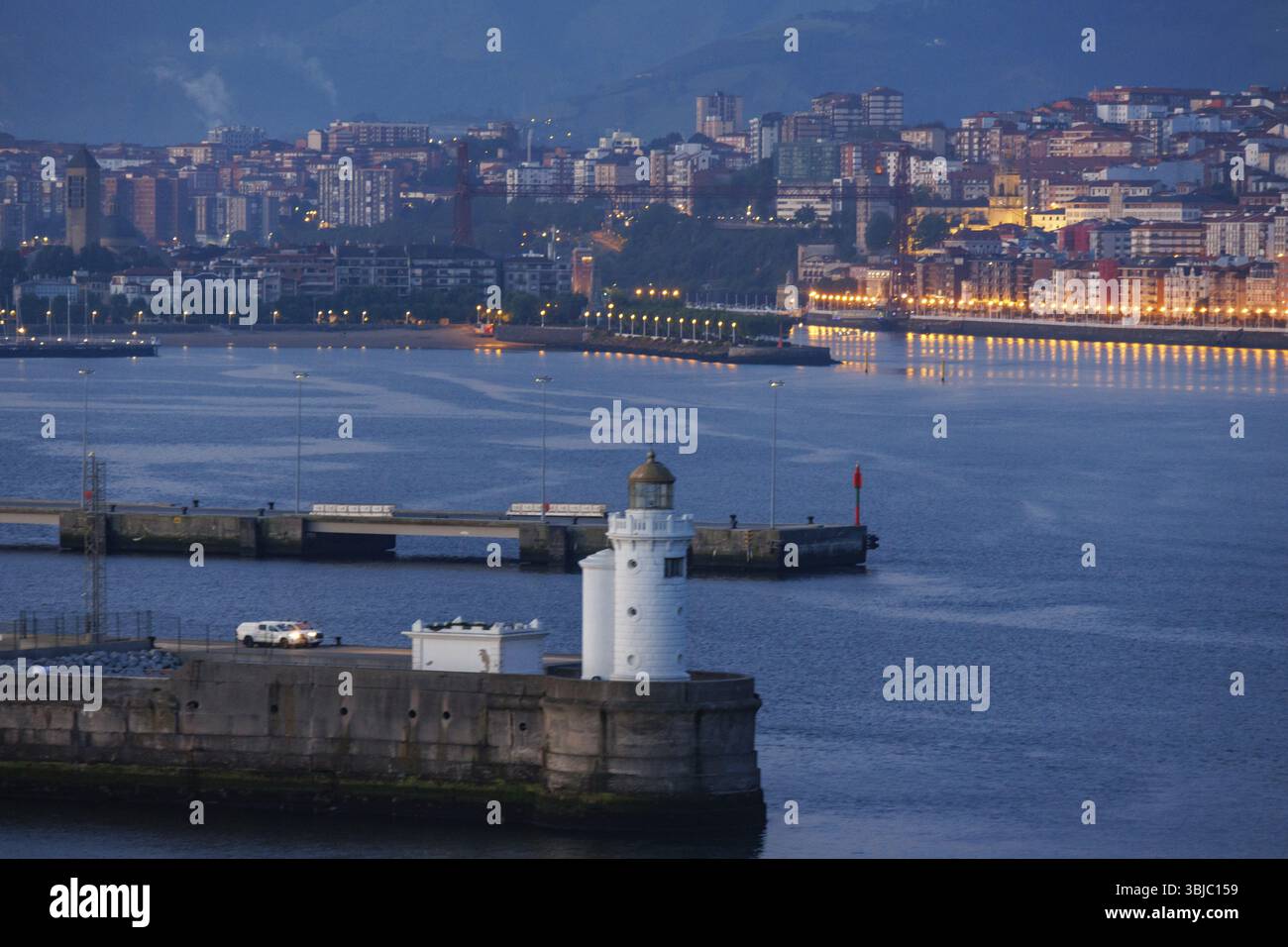 Un faro sull'acqua con una città illuminata sullo sfondo di notte, Gexto, Paesi Baschi, Spagna, Europa Foto Stock