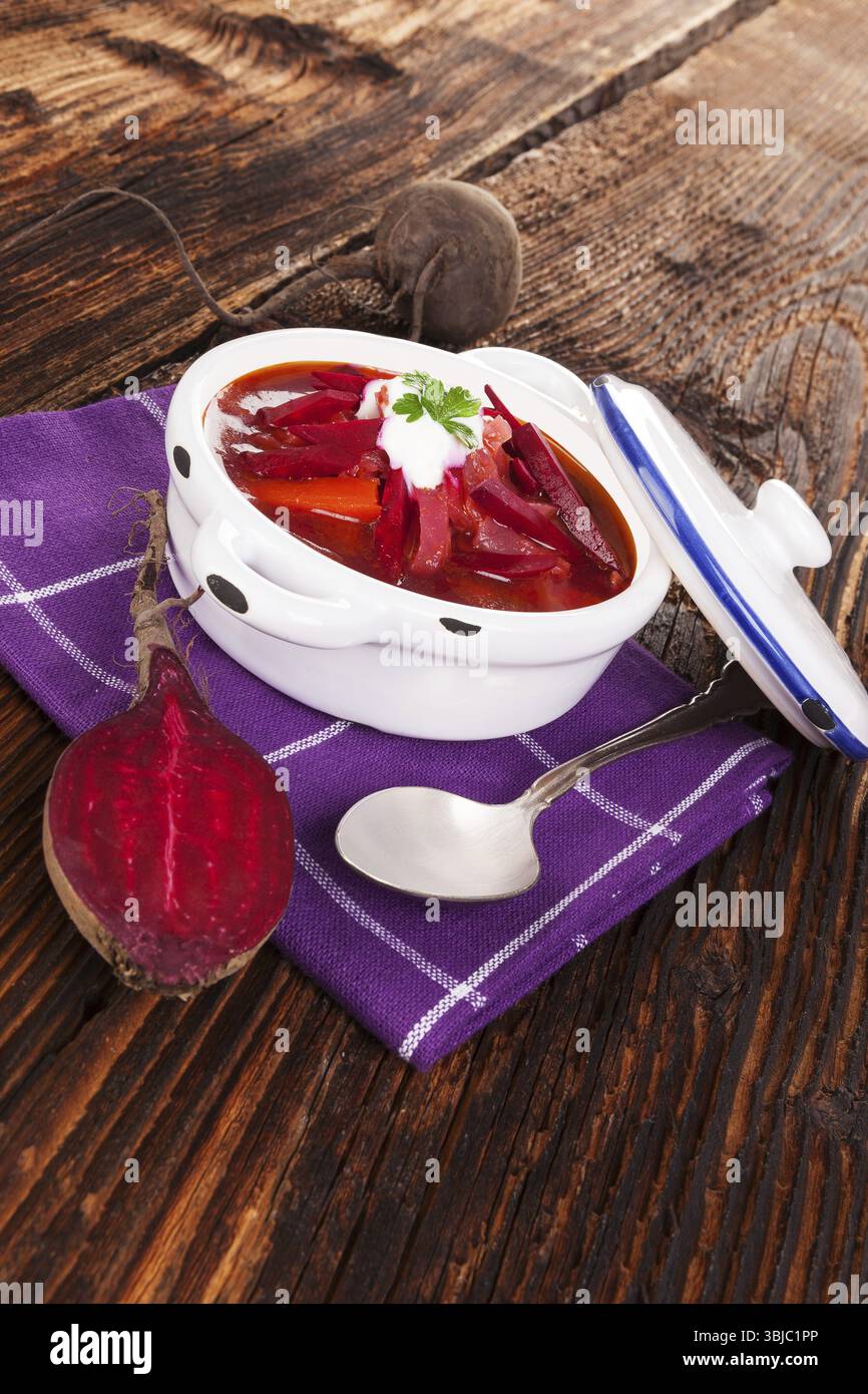 Deliziosa zuppa borsch ucraina con verdure fresche di barbabietola su un panno viola su un tavolo rustico in legno. Cucina tradizionale europea Foto Stock