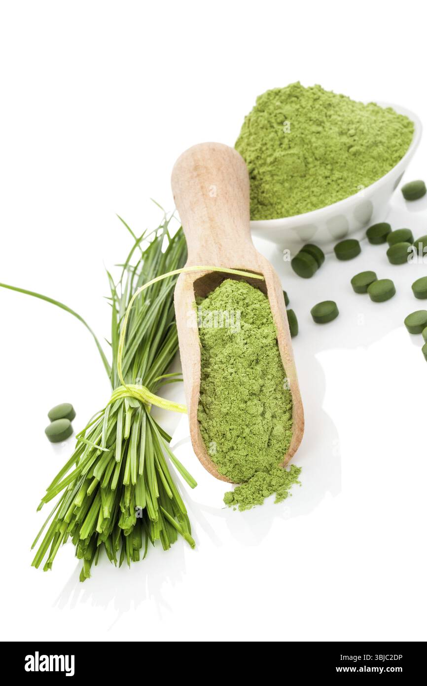 Medicina alternativa biologica a base di erbe naturali. Supercibo. Polvere di graminacee, lame e pillole verdi su paletta in legno e ciotola bianca isolata su bianco. Lui Foto Stock