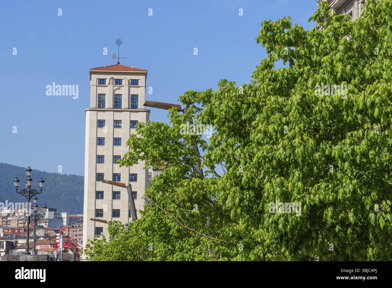 Un unico edificio a torre sorge nel cielo dietro alberi verdi, Bilbao, Paesi Baschi, Spagna, Europa Foto Stock