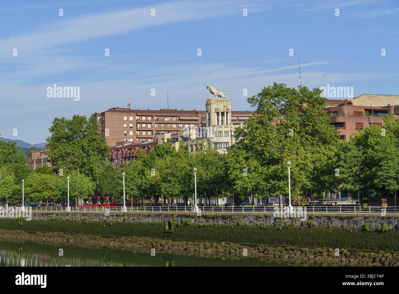 Lungo il fiume urbano con edifici e alberi verdi sotto un cielo limpido, Bilbao, Paesi Baschi, Spagna, Europa Foto Stock