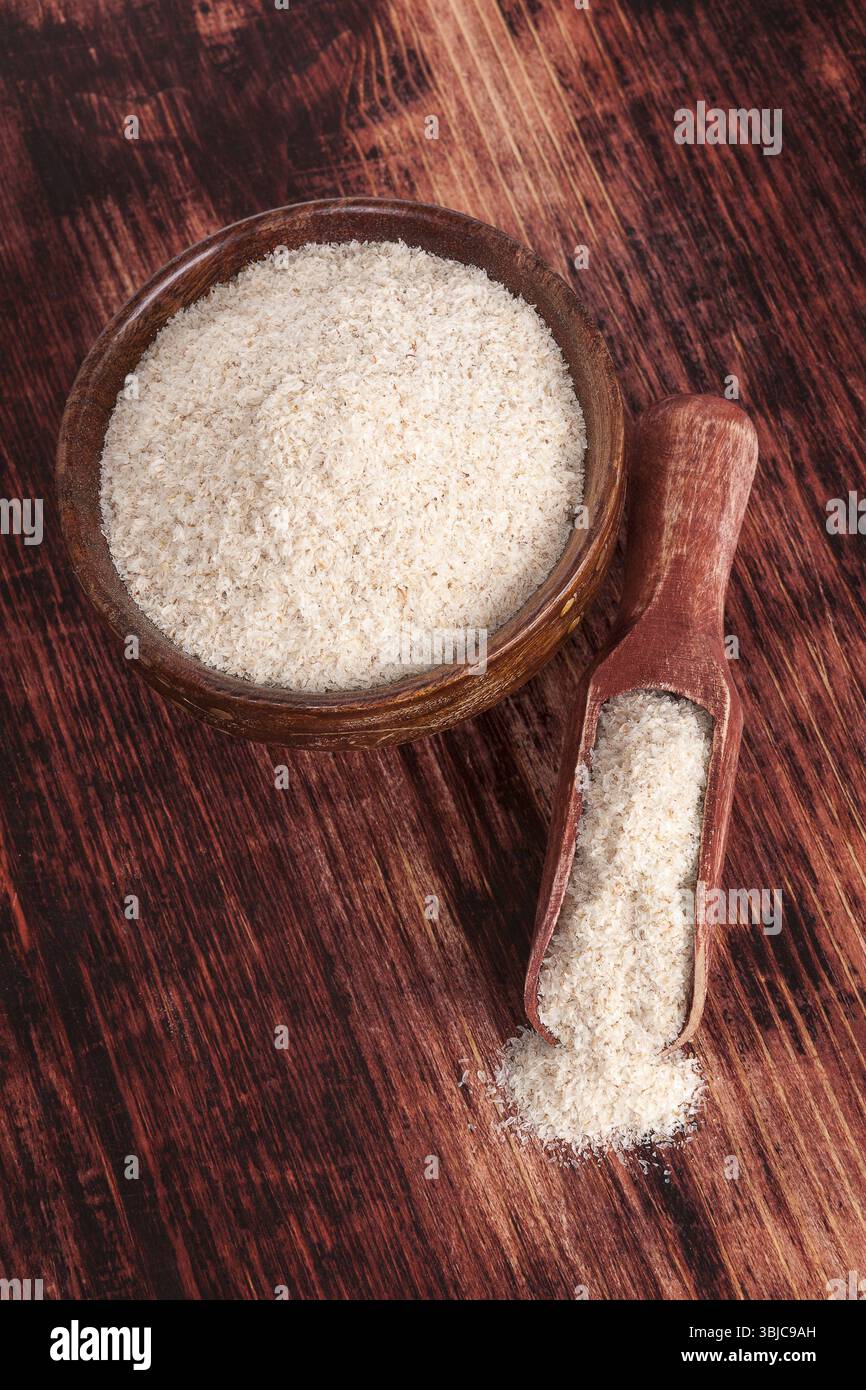 Psicllium in fibra alimentare in ciotola rotonda di legno su sfondo marrone scuro in legno, vista dall'alto. Concetto di alimentazione sana Foto Stock