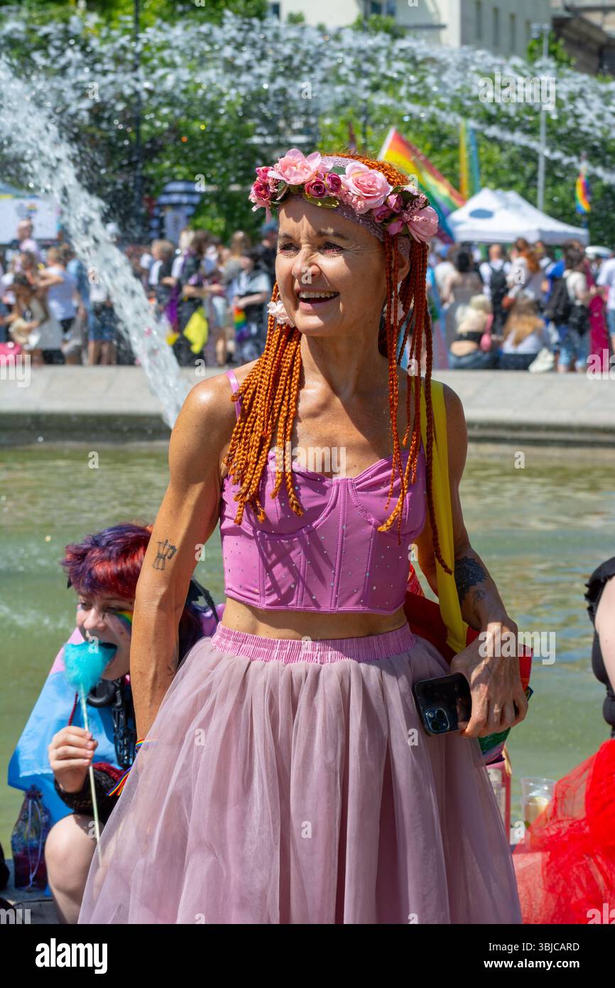 Una donna che indossa una corona di fiori e un tutù rosa sorride accanto a una fontana durante la Parata dell'orgoglio di Varsavia al Giardino Sassone di Varsavia, Polonia, nel giugno 2025. Foto Stock