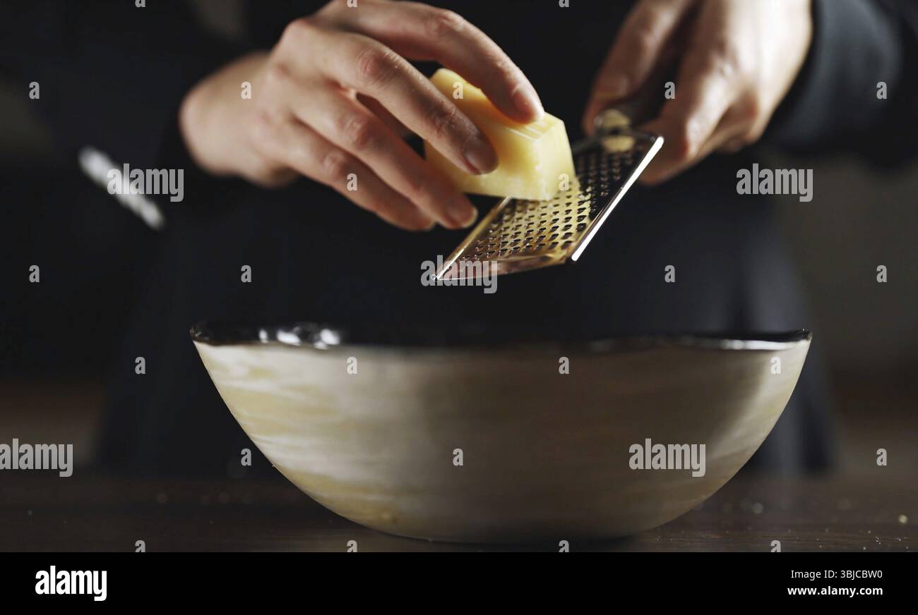 Donna che grattugia il formaggio su una grattugia in cucina Foto Stock