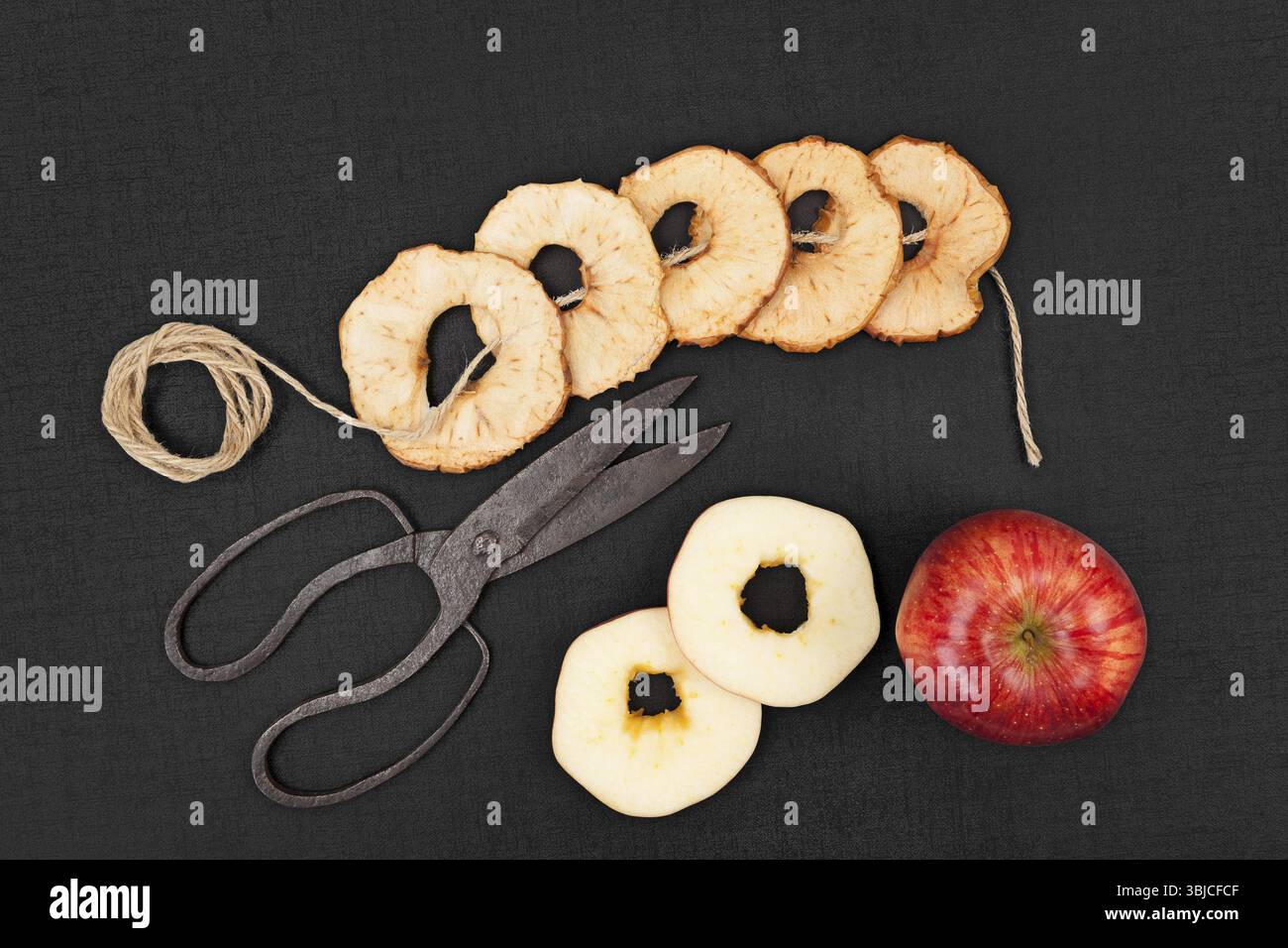 Mele asciutte e fresche su sfondo nero, con vecchie forbici vintage e cordoncino marrone naturale. Alimentazione sana, conservazione del raccolto stagionale Foto Stock