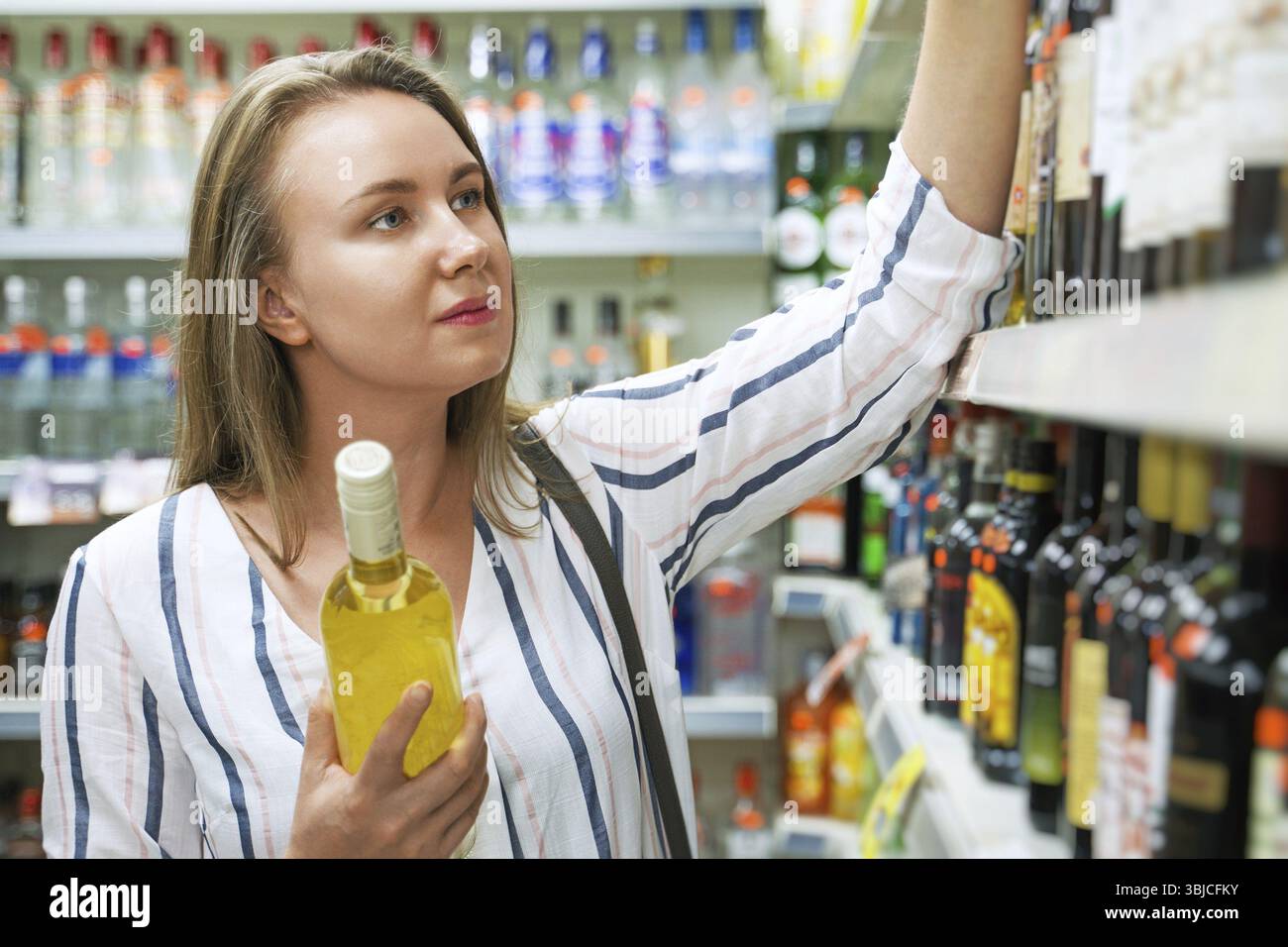 Bella donna che sceglie il vino bianco al supermercato Foto Stock